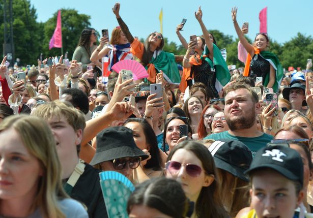 An image of crowds of people at a music festival cheering and filming on their mobile phones.