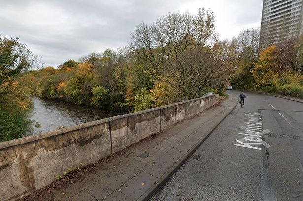 An image of a road bridge over a river, with a block of flats visible in the distance.