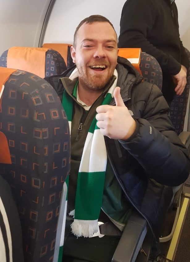 Kevin Davidson smiling with thumbs up in airplane seat with Northern Ireland scarf on