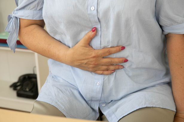 An older woman in a blue shirt is experiencing stomach pain, which is indicative of digestive issues, specifically constipation.