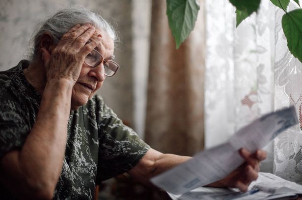 Senior woman with grey hair and in glasses holding hand on forehead showing feeling of desperation. Lady scared to have money problems after paying monthly bills that grow uncontrollably every month.