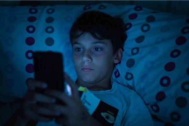 Child in bed at night with a book and a smartphone in the dark. 