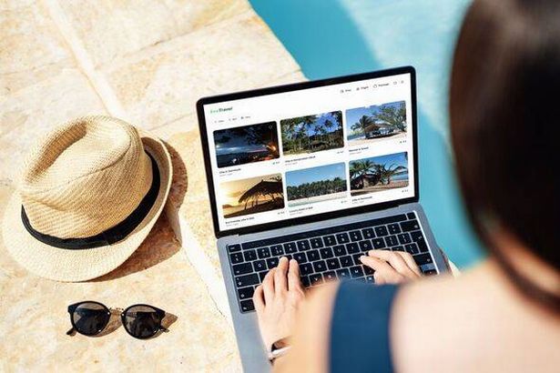 Over the shoulder view of young woman booking holiday accommodation via laptop by the pool