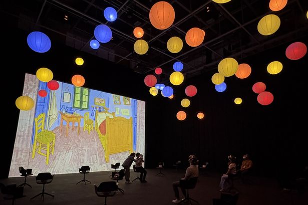 Room with people wearing VR headsets, Vincent Van Gogh work on the wall and hanging orb lights