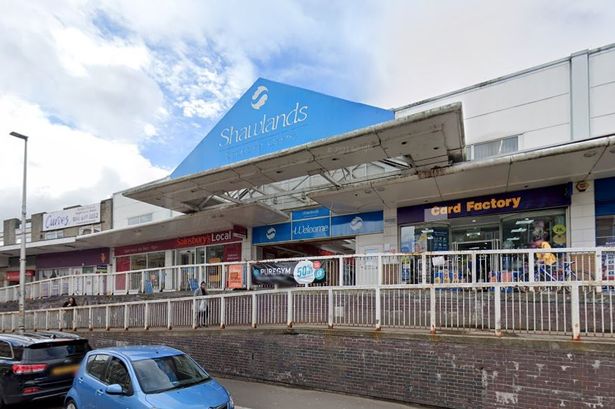 An image of the exterior of a shopping centre, with a blue sign above the door and entrances to shops on the outside.