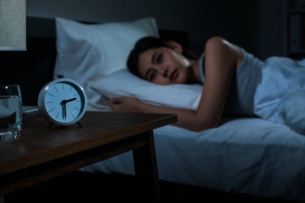A stressed young woman lying awake in bed, struggling with insomnia and restlessness.