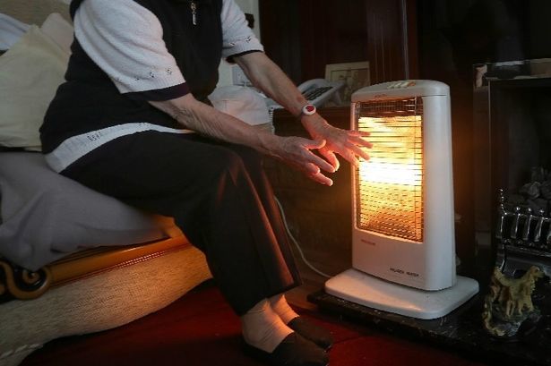 An elderly person in front of a heater