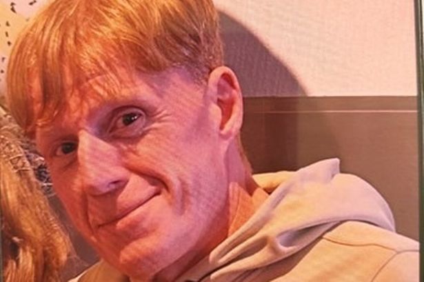 An image of a middle-aged red-haired man wearing a light coloured hooded top.