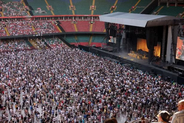 A crowded stadium as people stand looking towards a large empty stage