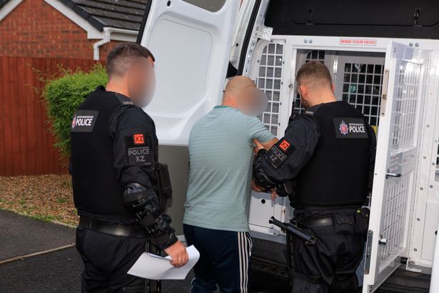 A suspect is taken to a police custody van following a raid in Irlam
