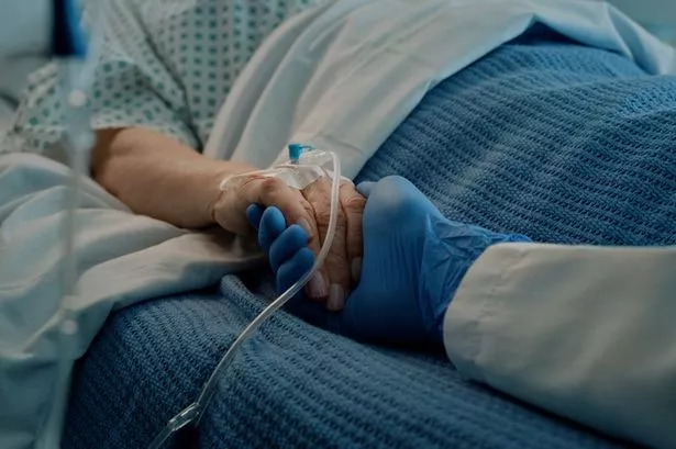 Patient and doctor holding hands in hospital bed after patient has undergone surgery, in hospital gown