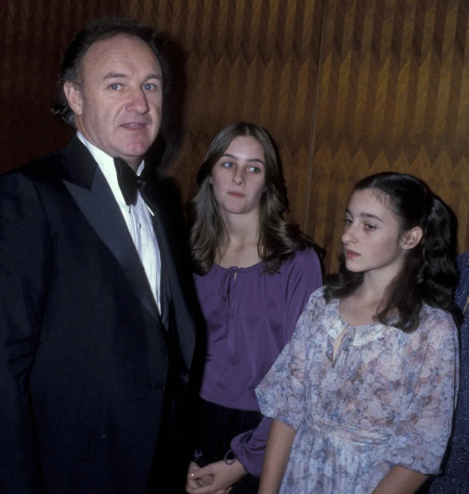 Man in tuxedo and a large bowtie stands next to two teenagers who are looking away.