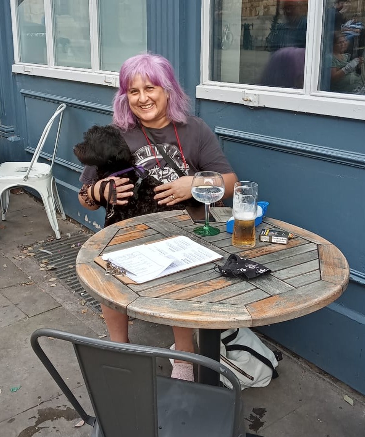 Woman with purple hair sitting outside a pub with her dog.