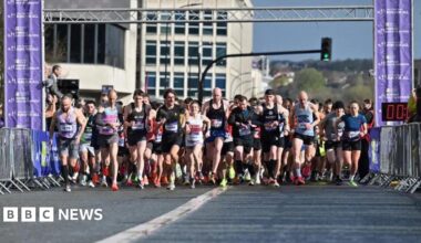 A large group of runners at the start line of the Sheffield Half Marathon in 2024. They are mostly men in shorts and vests. It is a sunny day.