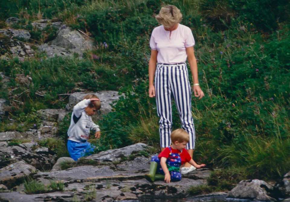 Princess Diana wearing striped pants standing on rocks with Prince Harry and Prince William at Balmoral