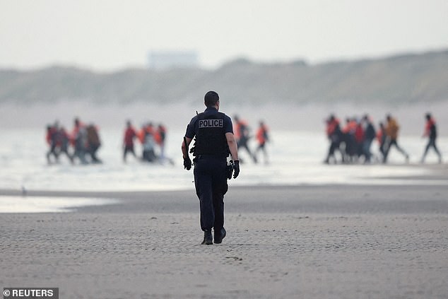 French police try to stop a group of migrants as they walk on the beach in an attempt to get on an inflatable dinghy on July 2