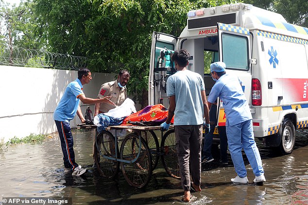 Pictured: A policeman and medics transferring bodies of victims onto an ambulance after the Air India Flight 171 crash