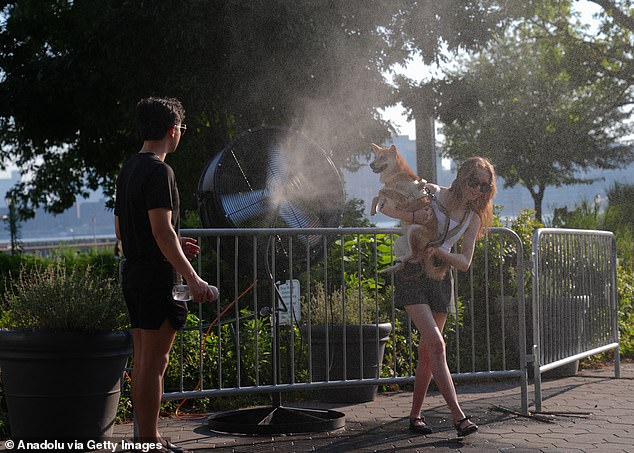 New Yorkers try to cool off with a fan that sprays water during a hot day as the National Weather Service on Monday issued a warning due to extremely high temperatures