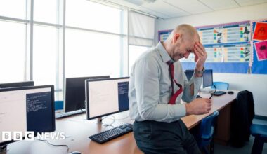 stock image of a stressed teacher holding his forehand in one hand and his glasses in the other.