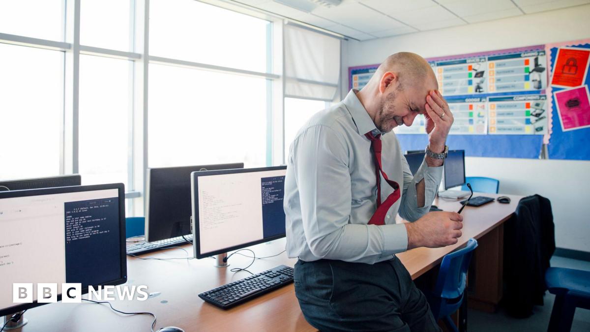 stock image of a stressed teacher holding his forehand in one hand and his glasses in the other.