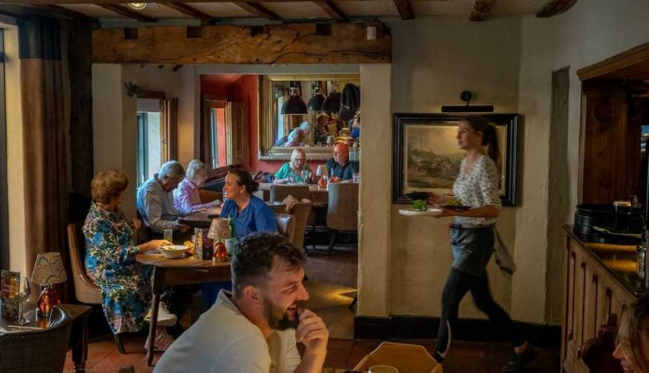 people sitting at tables inside restaurant; server carrying plates