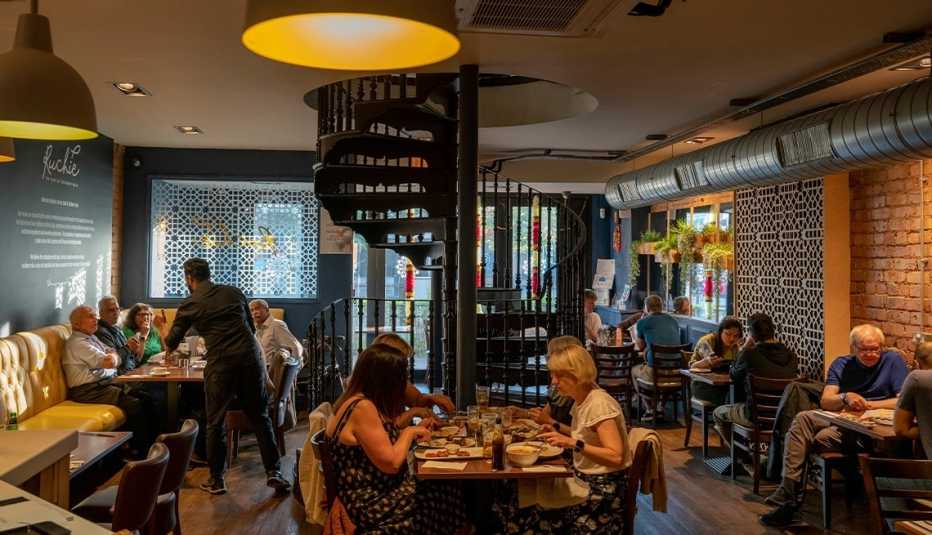 people sitting at tables inside restaurant; spiral staircase in middle leading up to another floor