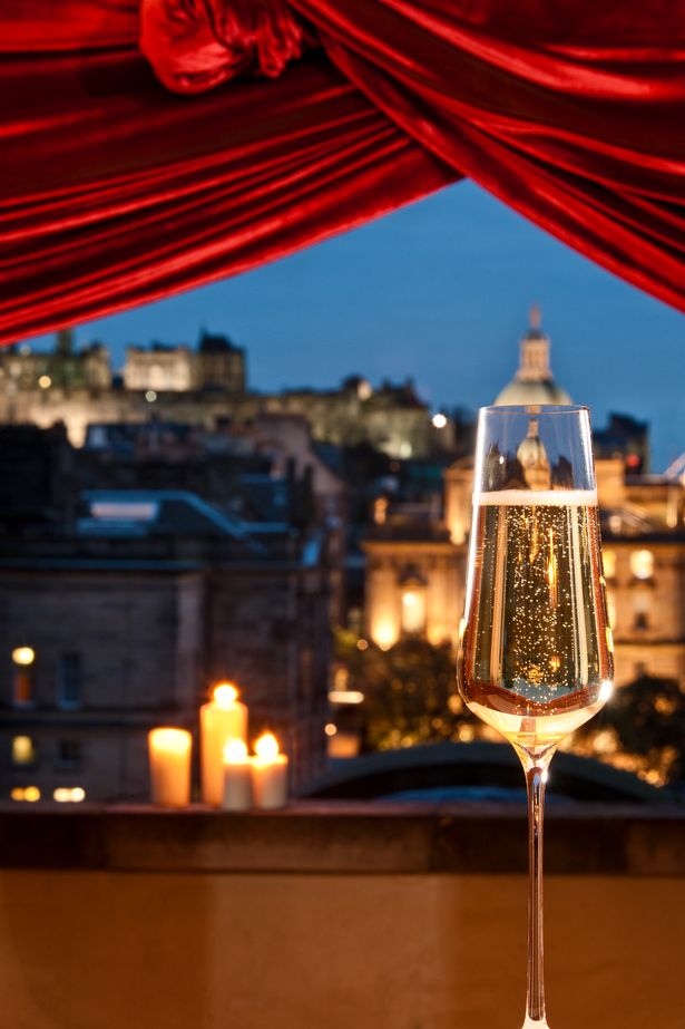 Glass of champagne inside hotel room overlooking Edinburgh skyline and castle at night