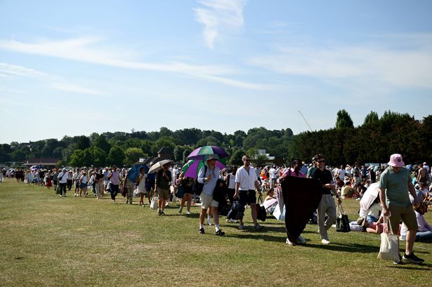 LONDON, ENGLAND - JULY 01: Hopeful spectators wait in the queue as they shelter from the sun under umbrellas on day two of The Championships Wimbledon 2025 at All England Lawn Tennis and Croquet Club on July 01, 2025 in London, England. (Photo by Hannah Peters/Getty Images)