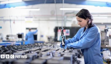 Female worker in blue overalls assembling components in circuit board assembly factory