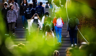 People walk up and down a staircase on a campus framed by greenery.