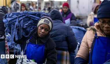 A woman, wearing a blue apron and black jersey, carries denim products in a garment factory in Lesotho