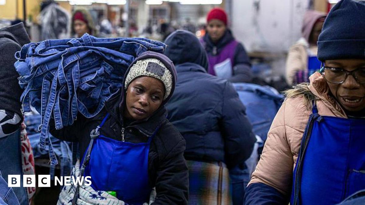 A woman, wearing a blue apron and black jersey, carries denim products in a garment factory in Lesotho