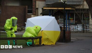 Two workers in bright yellow Hazmat suits crouch next to a forensic tent over a bench in Salisbury city centre