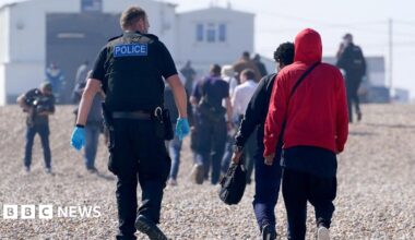 A police officer escorts a group of people thought to be migrants ashore from the Dungeness lifeboat in Dungeness, Kent, after being picked-up following a small boat incident in the Channel