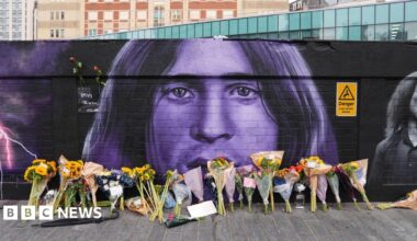 Floral tributes are left by the Sabbath mural, which is black and purple. Ozzy's likeness can be seen, with bunches of flowers lined up on the floor beneath it.