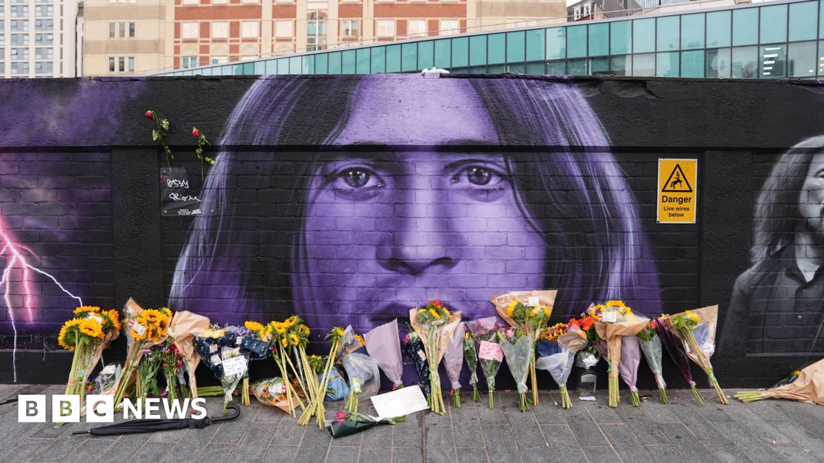 Floral tributes are left by the Sabbath mural, which is black and purple. Ozzy's likeness can be seen, with bunches of flowers lined up on the floor beneath it.
