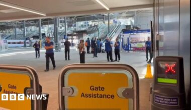 Yellow barriers blocking access to the platforms, with staff in the background.
