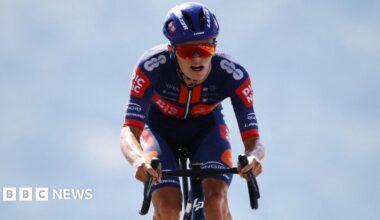 Cyclist Oscar Onley in blue and orange kit with a blue helmet and orange reflective sunglasses