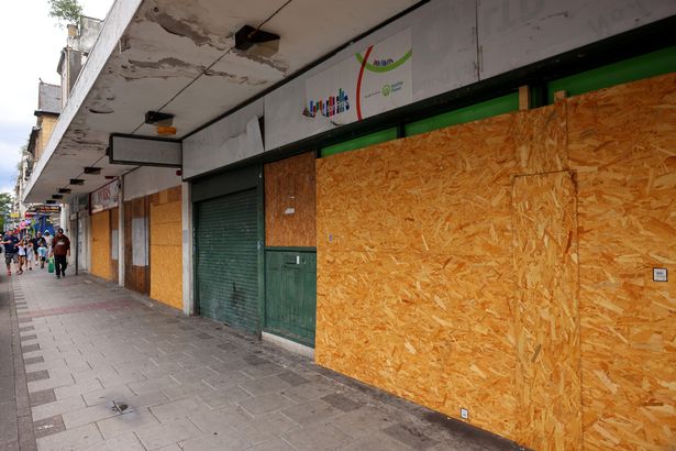 The image shows boarded up shops on the high street