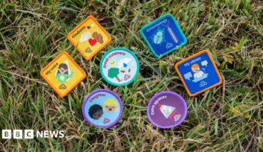Eight of the new badges laid out on the grass. They are: my voice, kindness, laughter, great outdoors, entomology, clam spaces and my views.