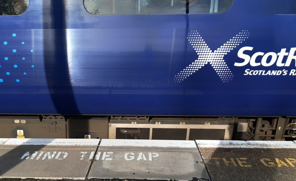 ScotRail train at a station platform with "Mind the Gap" painted on the platform.