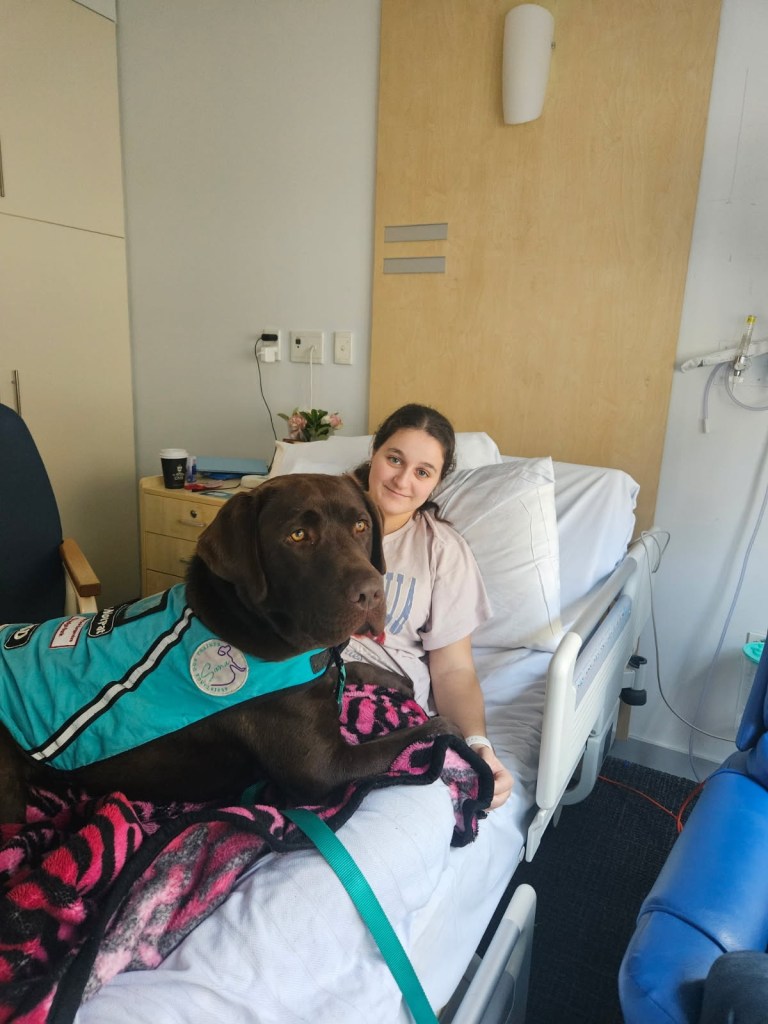 Young woman in a hospital bed with her service dog.