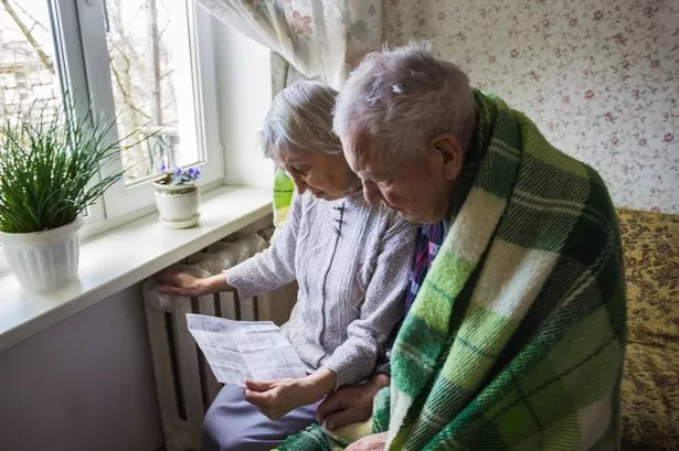 Senior woman holding gas bill in front of heating radiator