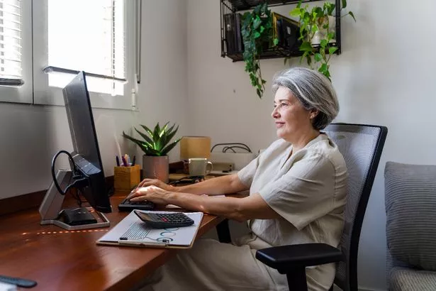 Mature businesswoman sitting at her desk at home, working on her computer and typing on the keyboard