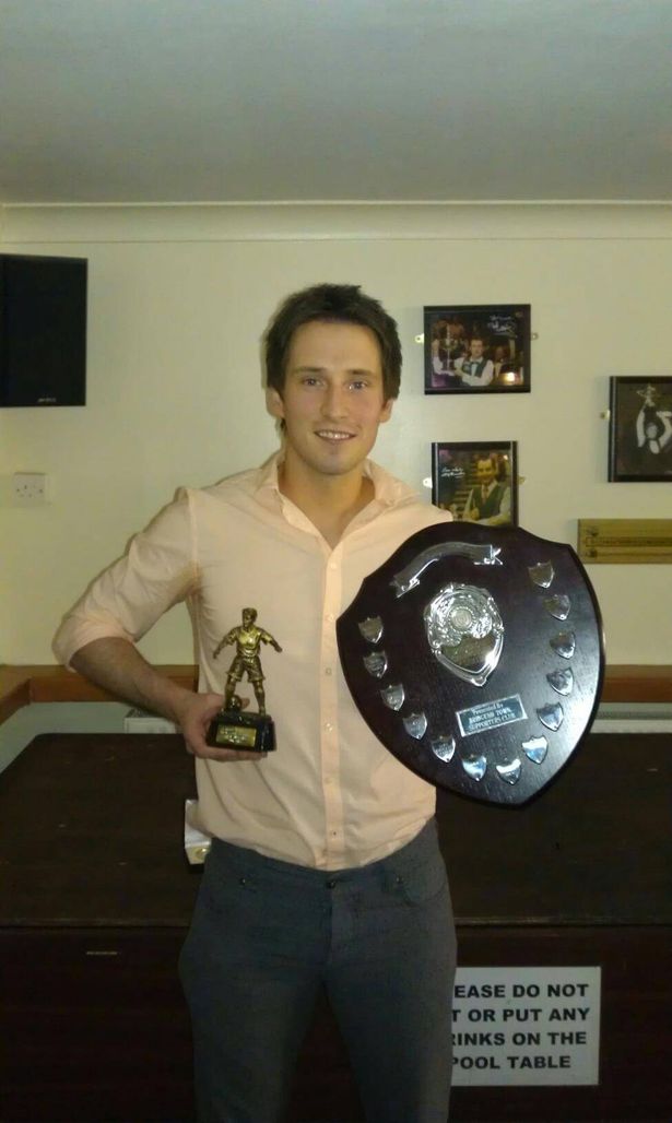 Picture showing a young Steven wearing a shirt and holding up a football trophy in one hand and a medal plaque in the other