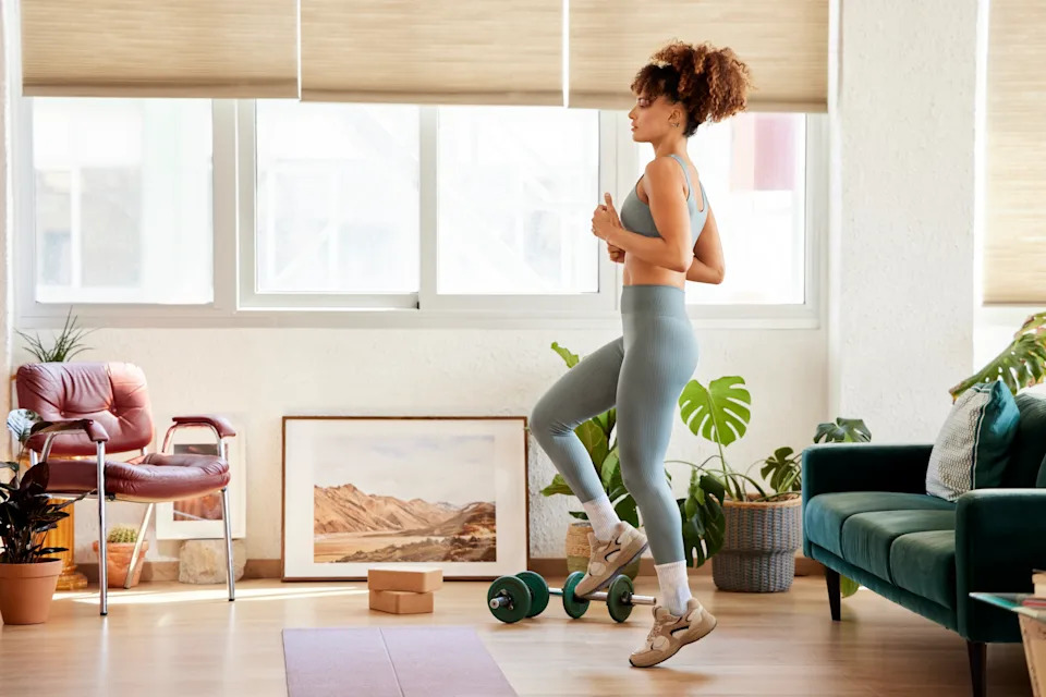 Full length of young woman doing warm up exercise. Woman is practicing in living room. She is at home