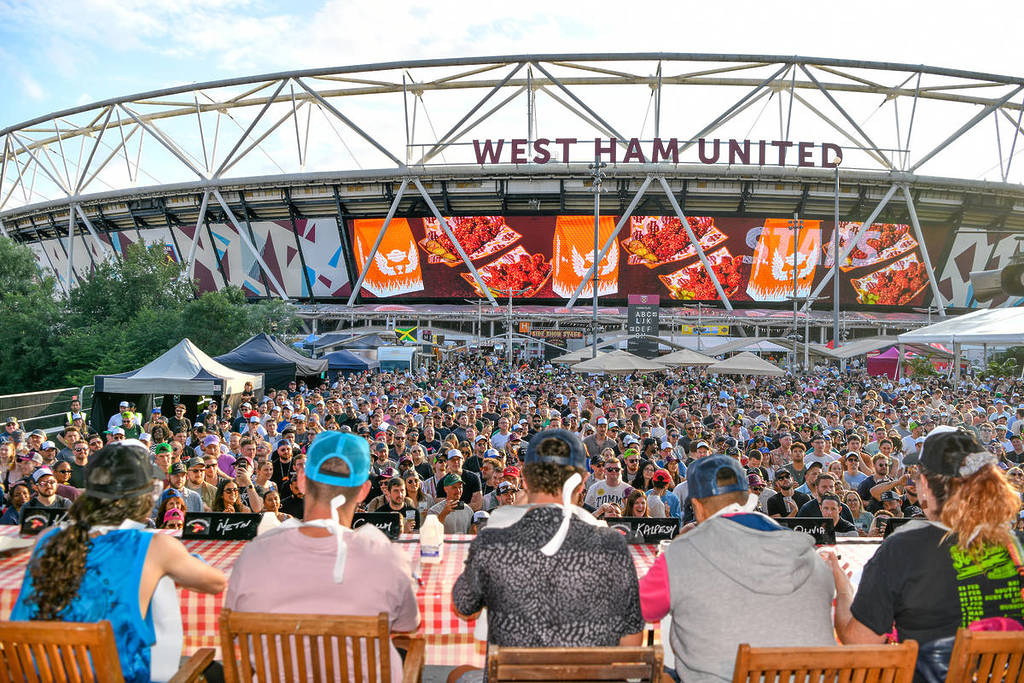 an eating challenge takes place in front of a crowd of on-lookers. in the background you can see the London Stadium.