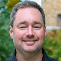 Ben Emery, Ph.D., has short blond hair, and is wearing a blue button-up shirt, smiling in a courtyard at OHSU.
