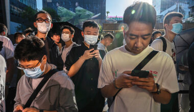 People look at their phones as they line up to buy Apple products outside a store in Beijing, China