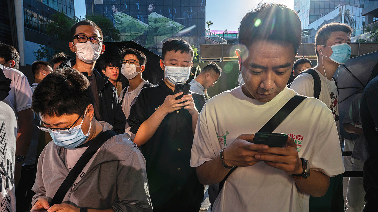People look at their phones as they line up to buy Apple products outside a store in Beijing, China